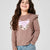 A young girl with long brown hair smiling, wearing a mauve-brown long-sleeve top with a sequined fox face graphic on the front, paired with blue jeans, against a light gray studio background.