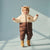 A toddler wearing a brown and cream bear-themed puffer snowsuit with a hood featuring bear ears and a small bear patch on the chest, standing against a light blue studio background.