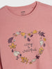 Pink shirt with leaf design and 'cozy & cheerful' text on a plain background