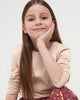 Young girl with long brown hair wearing a beige top against a white background