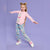 A young girl with blonde buns poses in a pink long-sleeve top with a white cat graphic and light blue pants featuring a repeating cat print, set against a solid lavender studio background.
