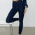 A model wearing dark blue high-waisted skinny jeans, sitting on a white stool with one leg bent up. The photo is cropped from the waist down against a clean, light gray studio background.