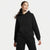 A woman modeling a black pullover hoodie and matching black sweatpants against a clean, light gray studio background.