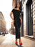 Woman in a black off-shoulder dress with red shoes standing on a city street.