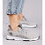 A pair of light gray knit athletic sneakers with black and white soles, shown on a model wearing light-wash blue jeans against a neutral gray studio background.