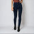 A model wearing dark navy blue high-waisted skinny jeans, paired with a rust-colored top and black ankle boots, standing against a light gray studio background.