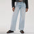 A person wearing light-wash wide-leg denim jeans, styled with a black leather jacket and black studded slide sandals, photographed against a clean white studio background.