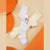 Three pairs of long socks laid flat on a beige background with orange abstract shapes. One pair is white with a small black face and brown ear detail, one pair is cream with a small brown paw print, and one pair are solid cream.