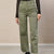A person wearing high-waisted olive green wide-leg jeans with a frayed hem, paired with a black lace long-sleeve top and black shoes, standing against a beige textured wall.
