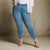 A model wearing high-waisted, blue skinny jeans with a white top and beige strappy heels, standing against a textured concrete wall.