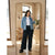 A woman takes a mirror selfie in a stylish room, wearing a light-wash blue denim jacket over a white top, black wide-leg pants, and black slide sandals.