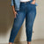 A person wearing high-waisted, ankle-length blue denim jeans with a fitted silhouette, styled with a light blue denim jacket and white top against a neutral indoor wall.