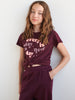 Person wearing a maroon t-shirt with text and matching pants against a white background