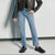A person wearing light-wash blue straight-leg jeans, a black leather jacket, black loafers, and pink socks, standing against a textured light gray wall.