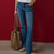 A model wearing blue flare jeans, holding a tan leather tote bag, standing against a solid dark red background.