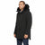 A man wearing a black hooded parka with a dark fur-trimmed hood, shown in profile against a plain white studio background.