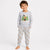 A young boy stands barefoot against a light gray studio background wearing a light gray long-sleeve pajama top with a forest and fox graphic, paired with matching gray pajama pants covered in a small brown and white animal print.