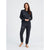 A woman modeling a matching dark gray lounge set consisting of a long-sleeve sweatshirt and jogger pants, standing against a light gray studio background.