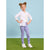A young girl with her hair in two buns stands on a green grass-like surface against a light blue background, wearing a white button-up shirt over a cream top, purple-and-white gingham leggings with white floral prints, and white sneakers.