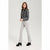 A woman modeling a dark gray textured jacket and light gray flared pants with black ankle boots, standing against a light gray studio background.