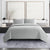 Quilted gray coverlet on a bed in a bedroom setting with framed artwork on the wall.