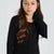 A young girl with long brown hair wearing a black ribbed button-up cardigan sweater, photographed against a light gray studio background.