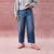 A person wearing blue wide-leg cropped jeans, a light gray sweatshirt, and pink sneakers, standing against a textured pink backdrop.