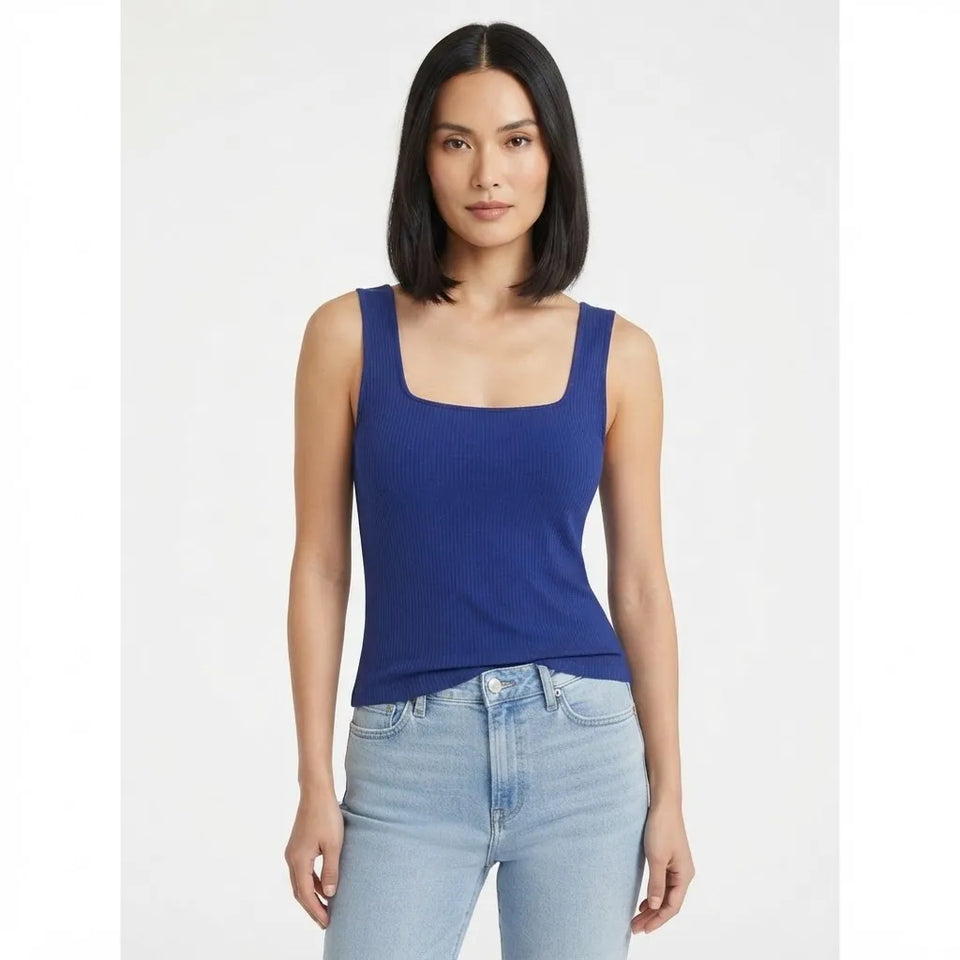 A woman modeling a royal blue ribbed tank top with a square neckline, paired with light-wash blue jeans, against a plain light gray studio background.