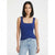 A woman modeling a royal blue ribbed tank top with a square neckline, paired with light-wash blue jeans, against a plain light gray studio background.