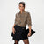 A woman modeling a leopard-print button-up blouse with three-quarter sleeves and a black wrap-style mini skirt, holding a black jacket against a plain light gray studio background.