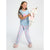 A young girl stands against a light gray studio background wearing a light blue pajama set with pink mermaid prints and holding a plush unicorn toy.