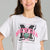 A young girl with her hair in two buns is wearing a light gray heather t-shirt with a large 'Michigan' graphic on the front in black and pink, featuring a green bear head logo.