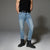 A model from the chest down wearing light-wash blue slim-fit jeans, a black tank top, and black boots, standing against a gray studio background.