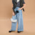 Child wearing a black leather vest, gray t-shirt, blue jeans, and holding a small handbag on a beige background