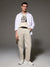 Man wearing a white shirt with text, beige vest, and pants on a gray background