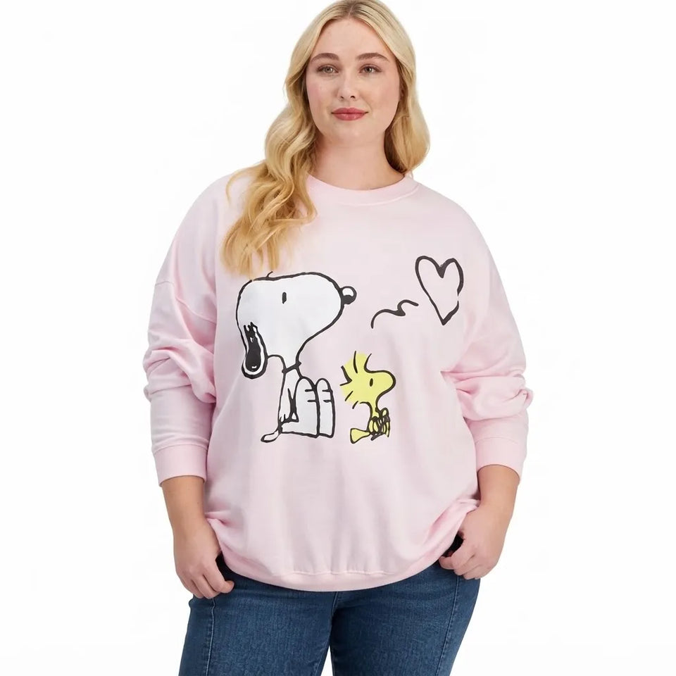 A woman wearing a light pink crewneck sweatshirt with a Snoopy and Woodstock graphic, paired with blue jeans, against a plain white background.