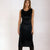 A woman modeling a sleeveless black velvet midi dress with a draped neckline and gathered waist details, set against a plain light background.