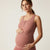 A pregnant woman wearing a dusty rose maternity tank top and matching leggings, posing against a solid light beige background.
