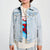 A young boy with brown hair wearing a light wash blue denim jacket over a cream graphic t-shirt featuring Spider-Man, standing against a plain light gray background.