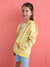 Young girl wearing a yellow striped hoodie against a pink wall