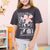 A young girl with blonde hair smiling, wearing a dark charcoal gray graphic t-shirt with a pink flower and the text 'FOCUS & TAKE CARE OF YOUR INNER SELF', paired with light gray sweatpants in a decorated children's room.