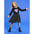 A young girl with curly blonde hair wearing a black long-sleeve dress with a sequined heart on the chest and a black tulle skirt with silver star patterns. She is wearing black boots with purple laces and posing against a solid blue studio background.