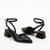 A pair of black pointed-toe slingback heels with block heels and ankle straps featuring gold-tone buckle details, shown on a clean white background.