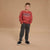 A young boy smiling and posing in a studio setting, wearing a rust-red crewneck sweatshirt with 'ATHLETIC ORIGINAL CITY' printed on the chest, dark gray jogger pants, and black sneakers with white soles, against a solid tan background.