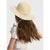 A child wearing a wide-brimmed straw sun hat with a pastel striped edge and a matching ribbon bow, shown from the back against a light gray background.