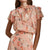 A woman wearing a peach pink ruffled blouse with a floral print in orange, cream, and gray, paired with a matching skirt against a plain white background.