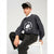A boy wearing a dark gray crewneck sweatshirt with a white circular graphic that reads 'Xavier Athletics Inc. 1996', paired with black jeans, a white collared shirt, and a gray baseball cap, sitting on a white stool against a light gray background.