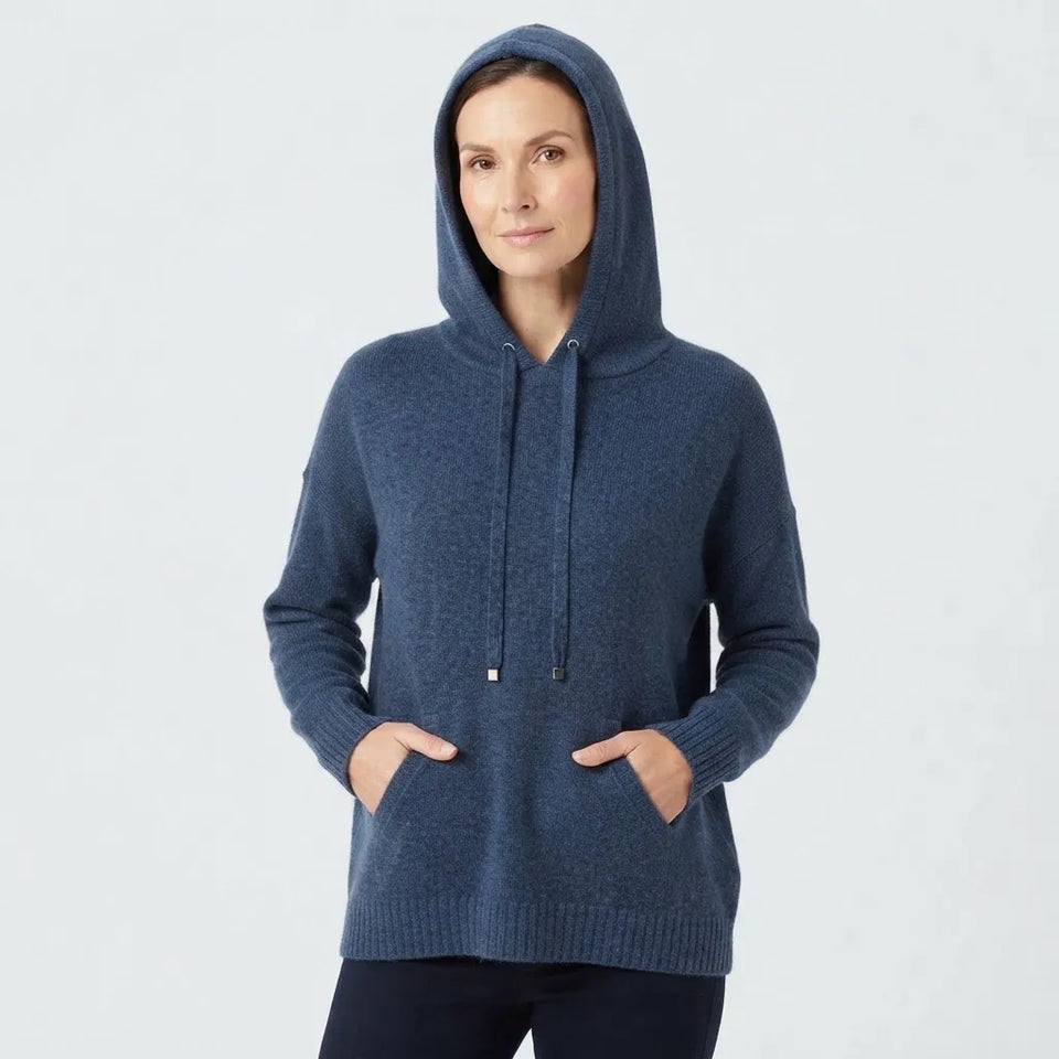A woman wearing a navy blue knit pullover hoodie with drawstrings and front pockets, standing against a light gray studio background.