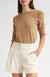 Woman wearing a brown top and cream shorts on a white background