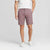 A man wearing dusty rose chino shorts, a white t-shirt, and white sneakers, standing against a light gray studio background.
